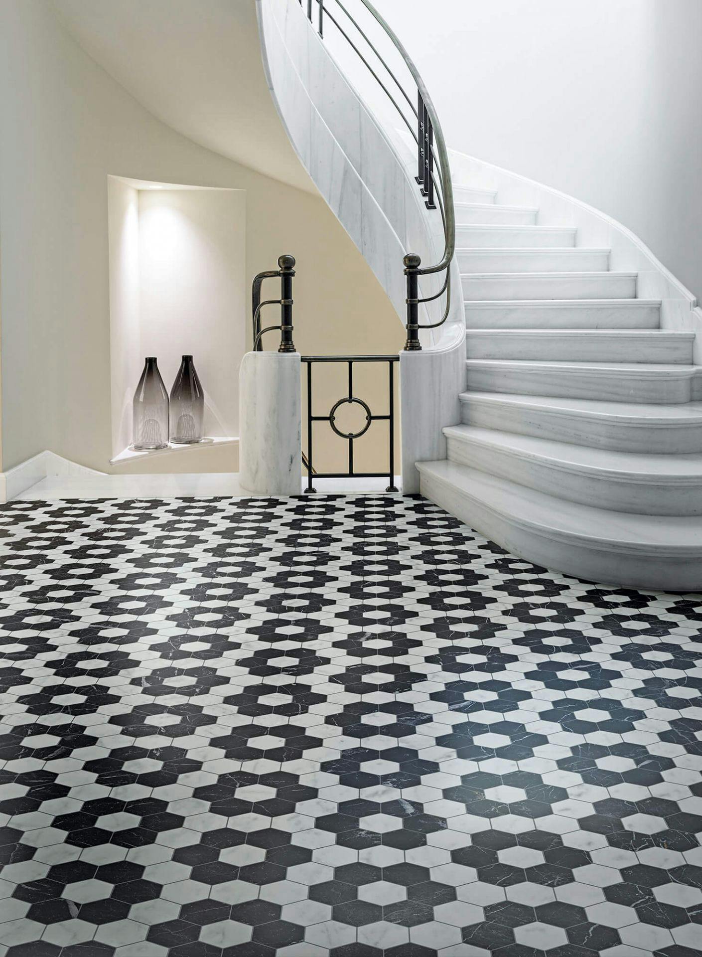 Entrada de casa estilo clássico com escadaria em caracol. Chão em mármore mate com padrão geométrico em preto e branco. Acabamento aveludado e sem reflexo. Bisazza, coleção Marmo Matt