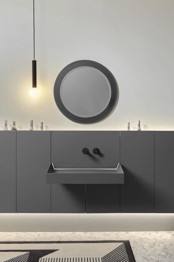 Composição de lavatório com armário, suspenso na parede, cor cinza, torneiras pretas. Espelho redondo na parede e candeeiro suspenso. Coleção Showdown de Antonio Lupi.